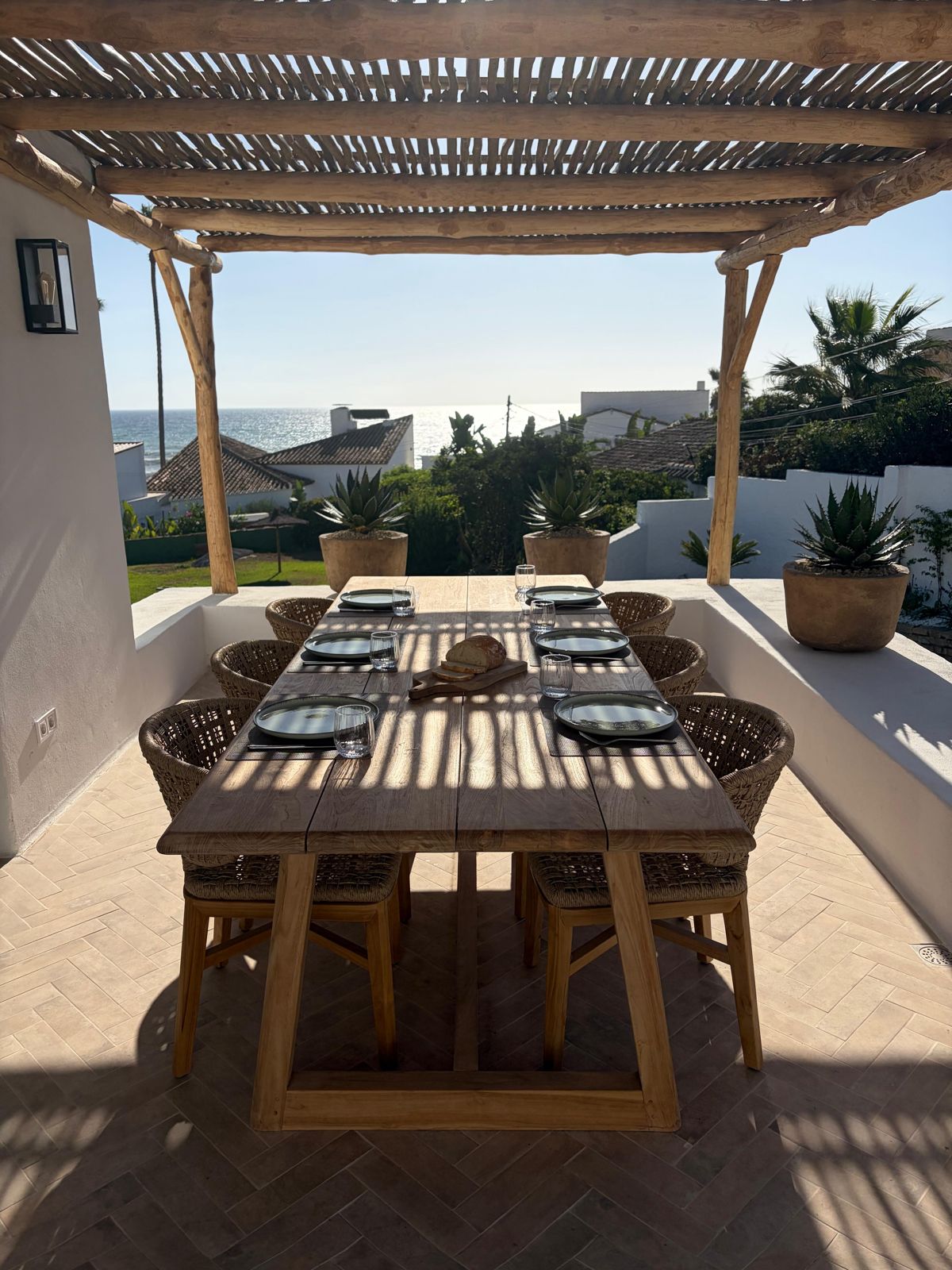 Eettafel onder de rieten pergola op het dakterras, met zicht richting zee